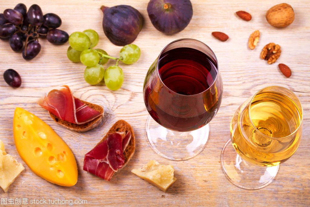 紅色和白色奶酪、 火腿、 無花果和葡萄與葡萄酒杯。木制的桌子上的酒杯。葡萄酒的靜物